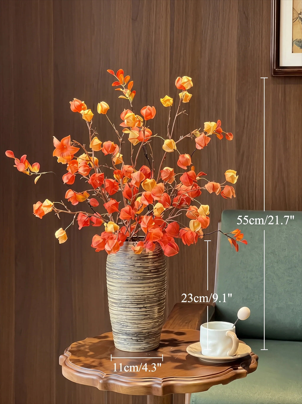 A decorative artificial floral arrangement in a ribbed gray ceramic vase, displayed on a wooden side table in a living room setting. White dimension lines overlay the image, showing the height of the arrangement as 55cm (21.