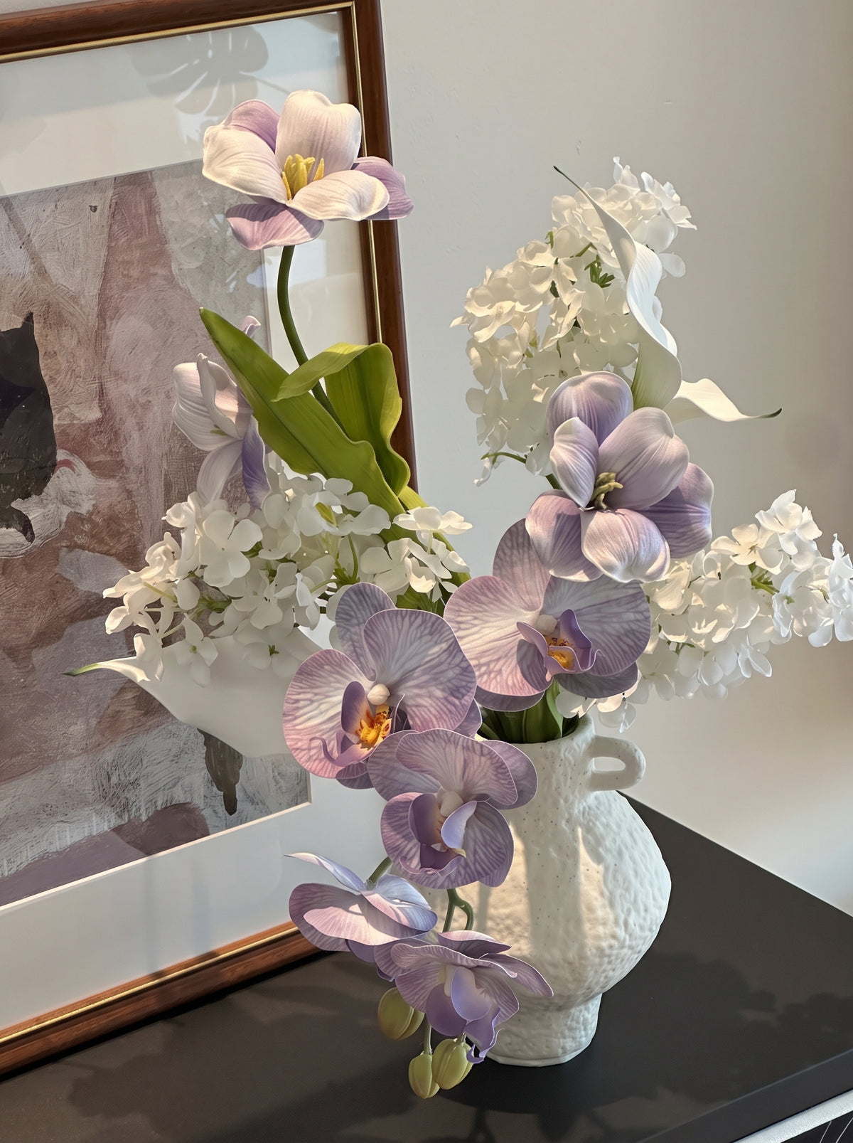 Eteriskt konstgjort blomsterarrangemang med lila orkidéer och tulpaner