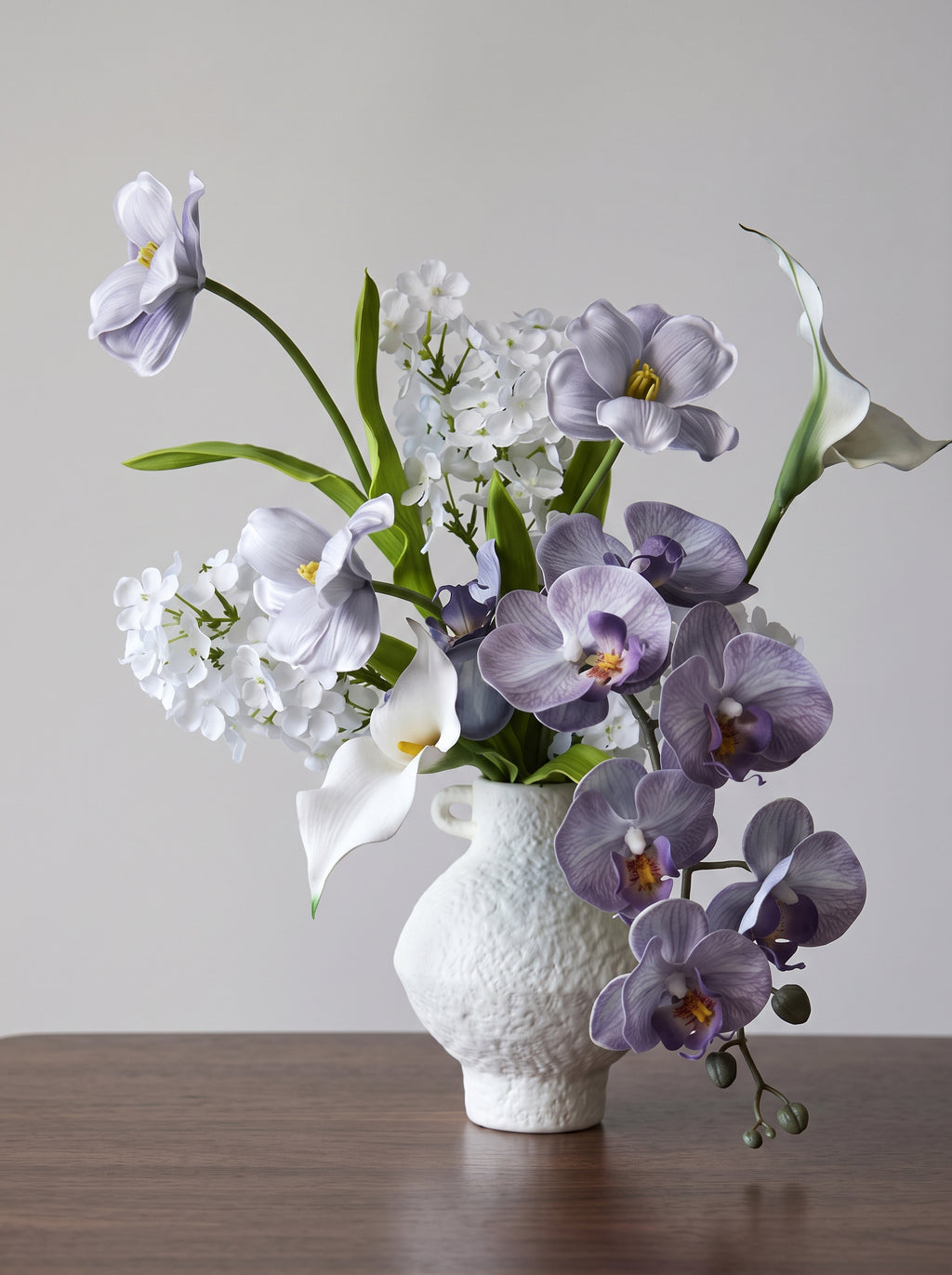 Eteriskt konstgjort blomsterarrangemang med lila orkidéer och tulpaner