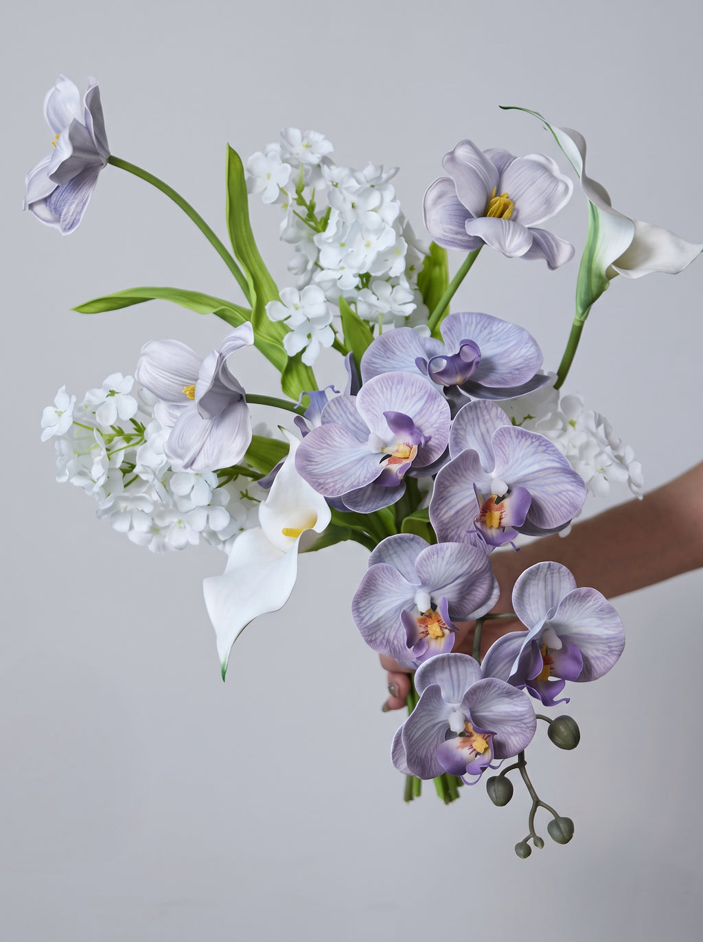 Eteriskt konstgjort blomsterarrangemang med lila orkidéer och tulpaner