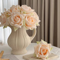 Beige vase with peach-colored roses on a table against a curtain background