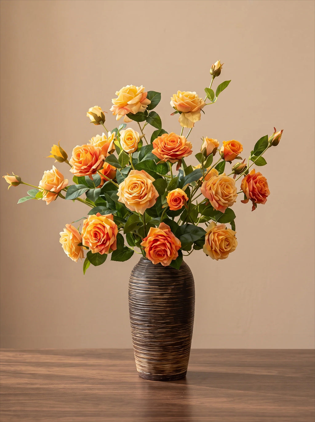 A bouquet of orange and yellow roses with green leaves arranged in a dark brown textured ceramic vase, set on a wooden table against a solid beige background.