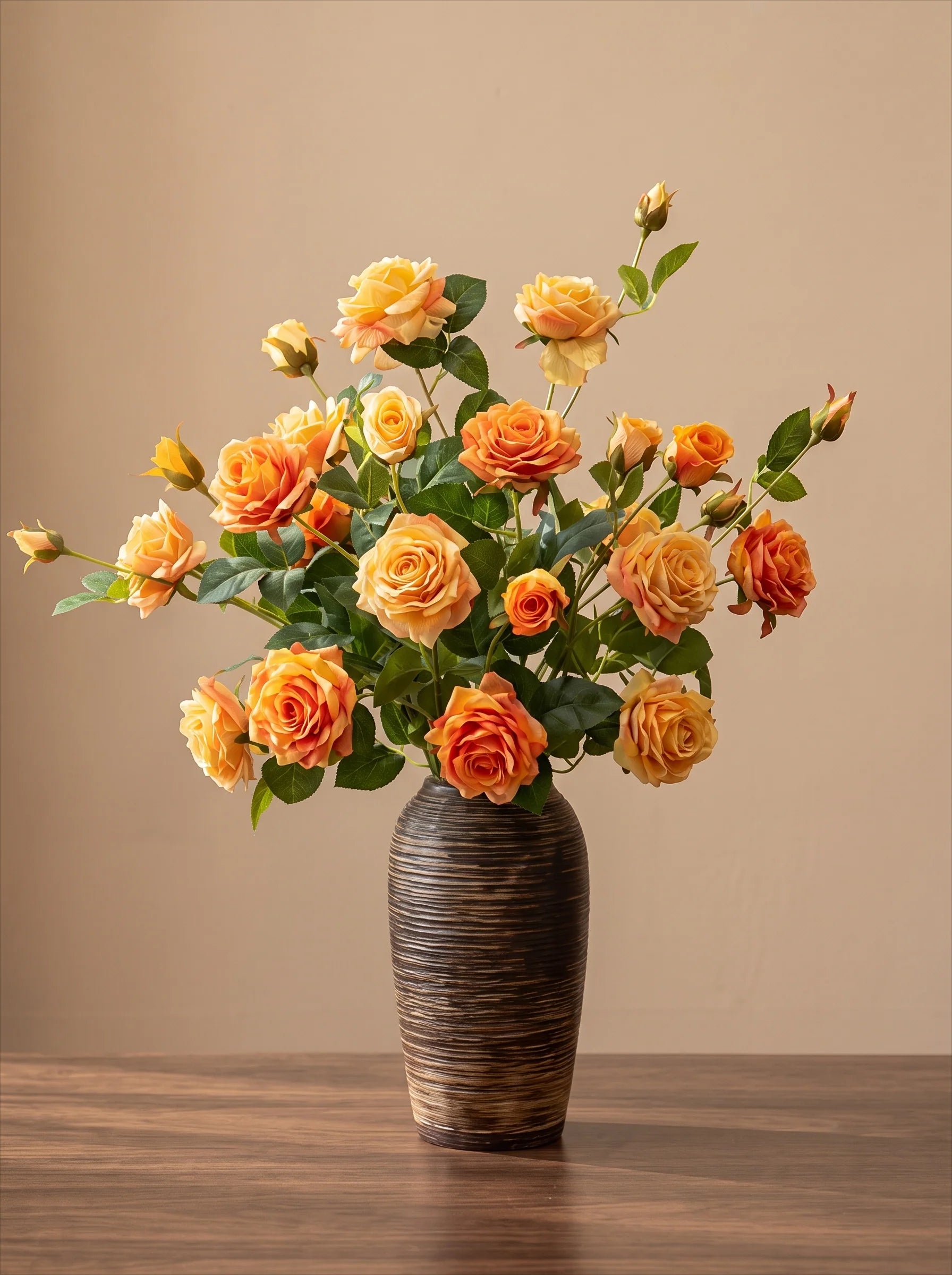 A bouquet of orange and yellow roses with green leaves arranged in a dark brown textured ceramic vase, set on a wooden table against a solid beige background.